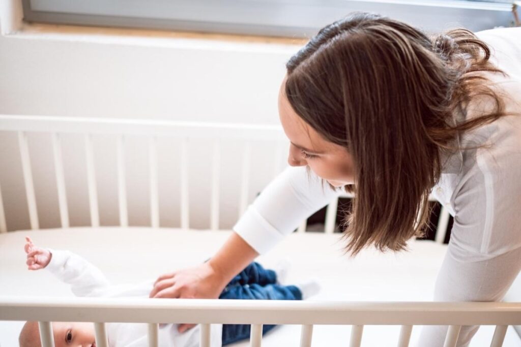 Mutter streichelt ihr Baby liebevoll im Gitterbett – Symbolbild für die Beratungspakete zu Stillen und Schlafen
